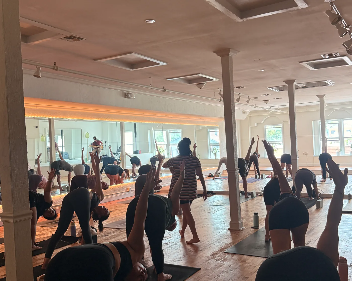 A yoga class in full flow on the main floor, reaching up toward the mirrored wall