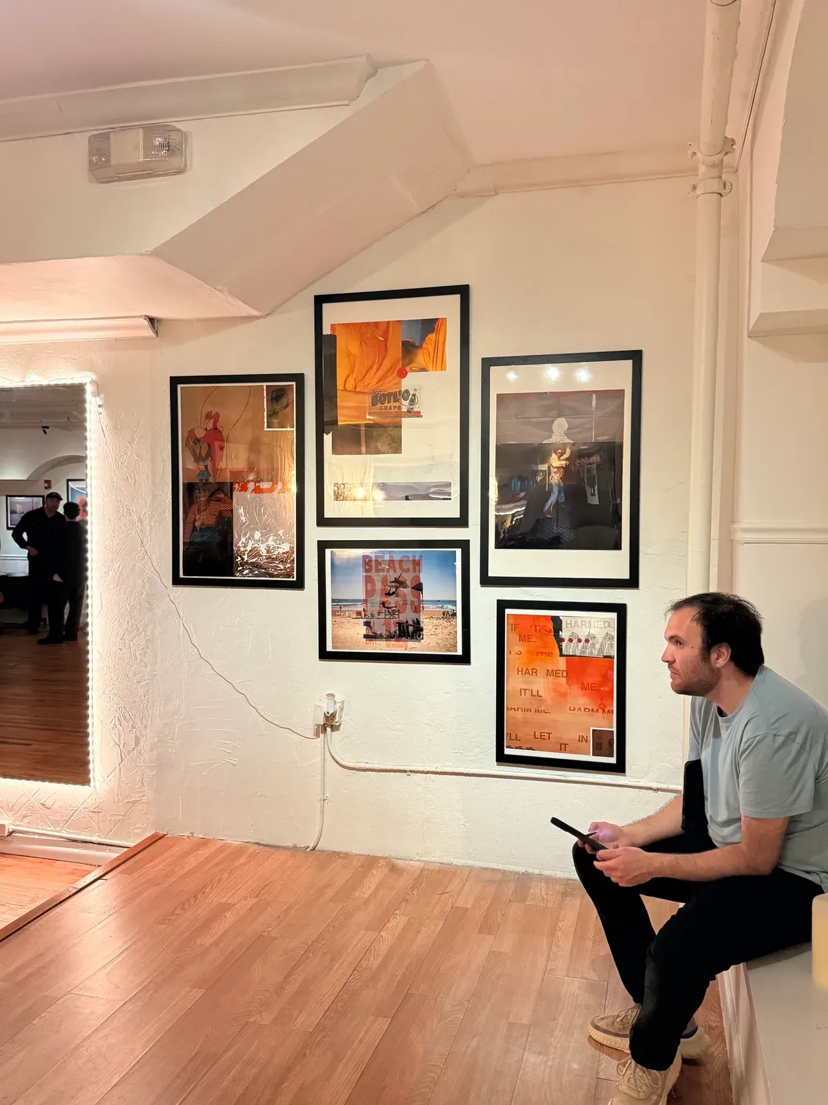 A visitor sitting below a wall of framed prints during an art exhibition